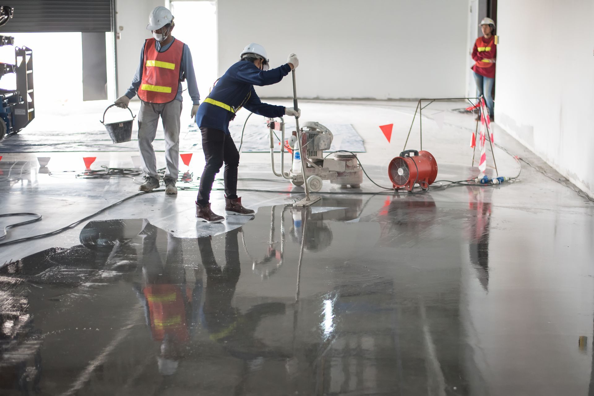 Workers using a floor grinder and squeegee to install industrial flooring.