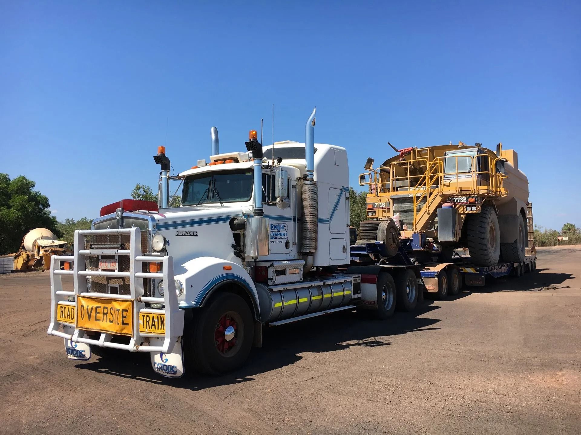 A White Truck is towing a yellow tractor — Ostojic Group in Berrimah, NT