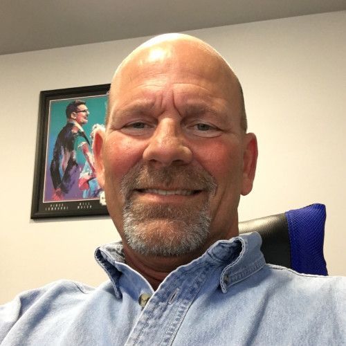 A bald man with a beard is smiling in front of a framed picture
