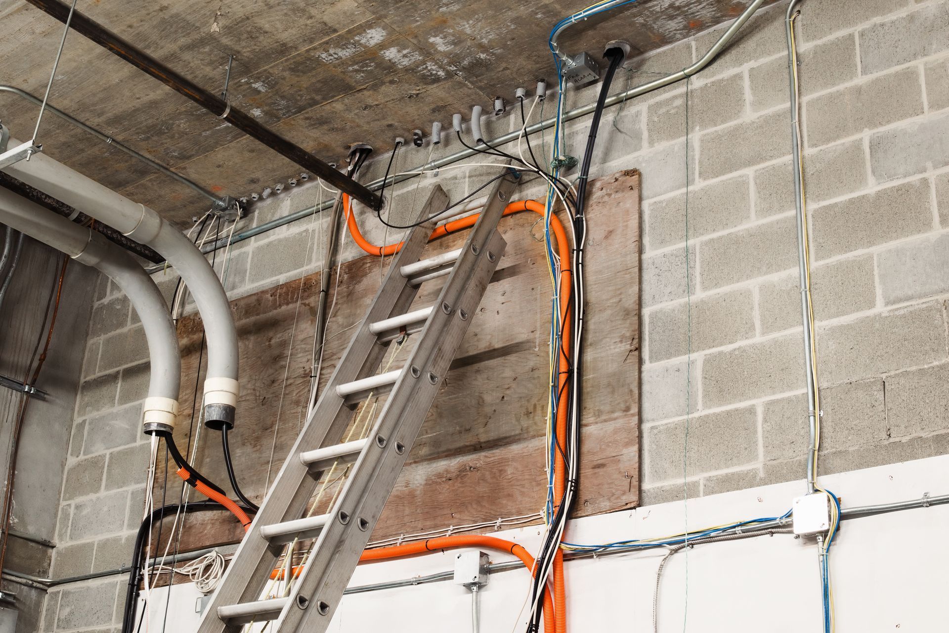 Ladder leaning against a brick wall with electrical wiring and conduits, likely under construction.
