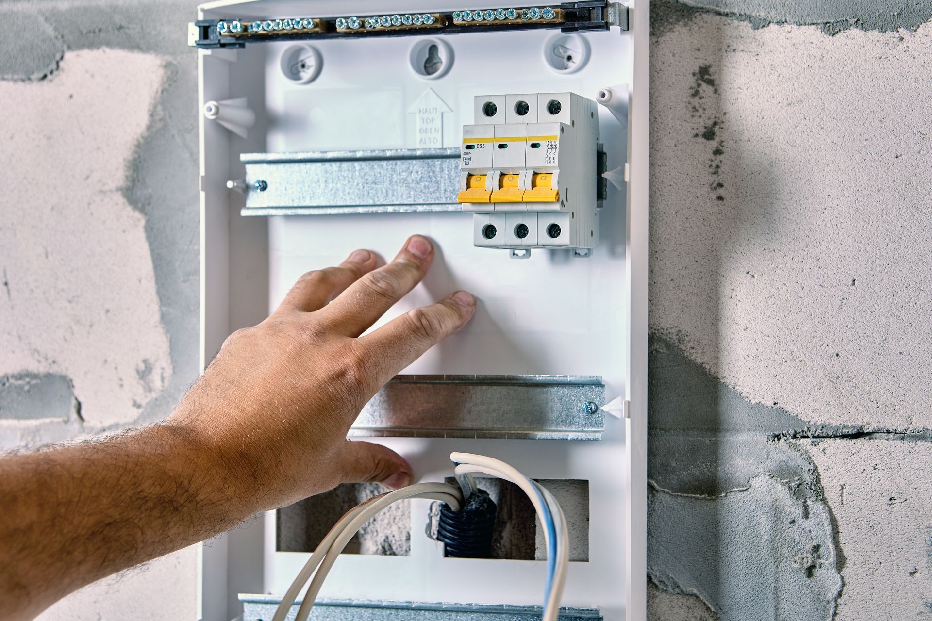 Hand touching electrical panel with circuits and wires in a partially built wall.
