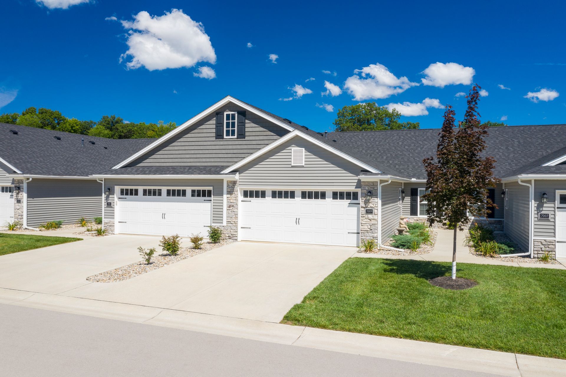 Row of attached gray houses with white garage doors and green lawns under a blue sky.
