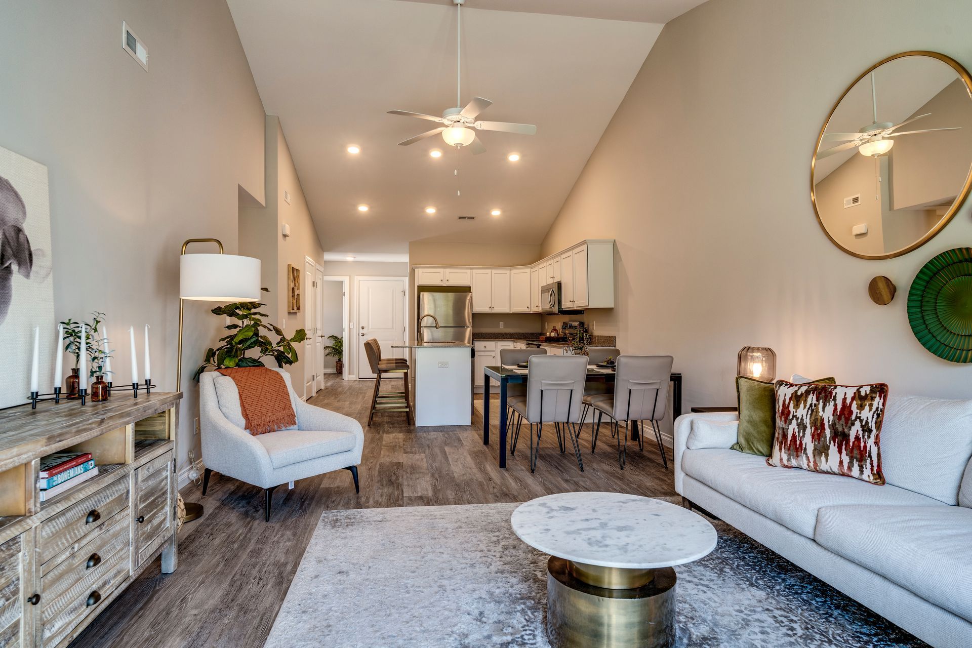 Living room with high ceilings, open to kitchen and dining area. White walls, wood floor, modern furniture.