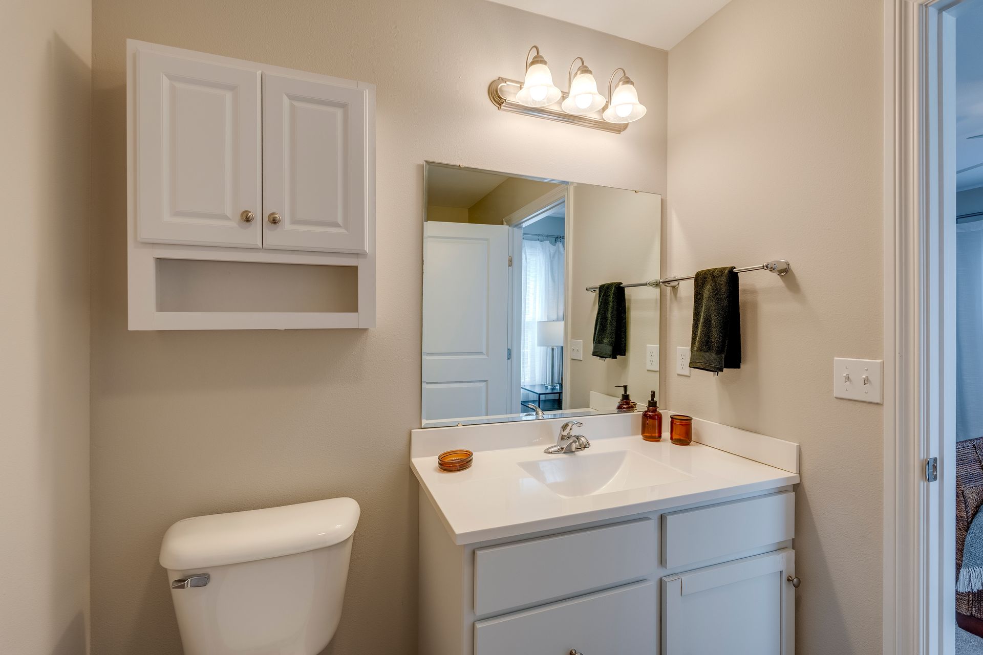 A small bathroom with a toilet, sink, mirror, and cabinet. White and neutral tones throughout.