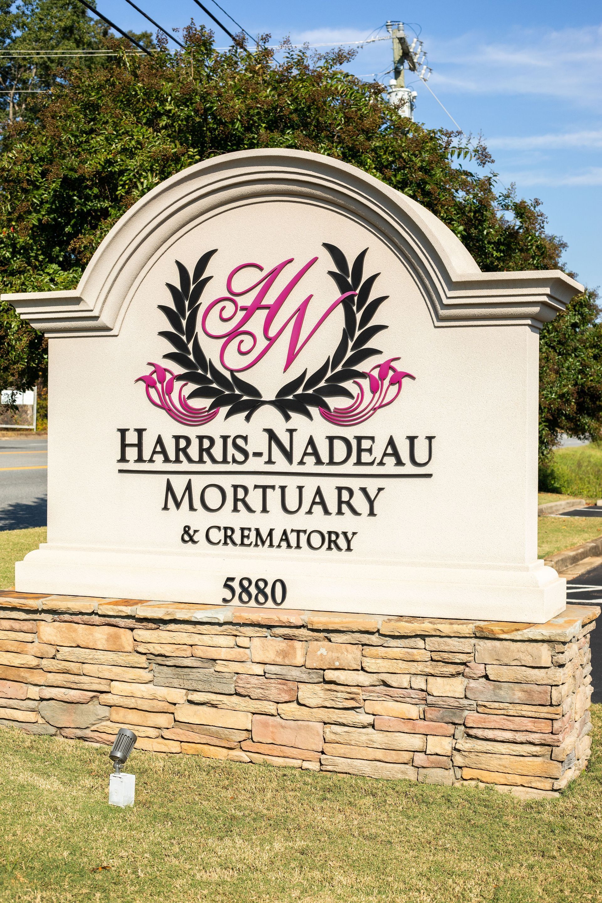 Sign for Harris-Nadeau Mortuary & Crematory, with logo and address 5880, on a stone base.