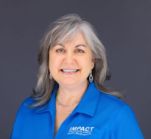 Woman with gray hair smiles, wearing a black top, against a light gray background.