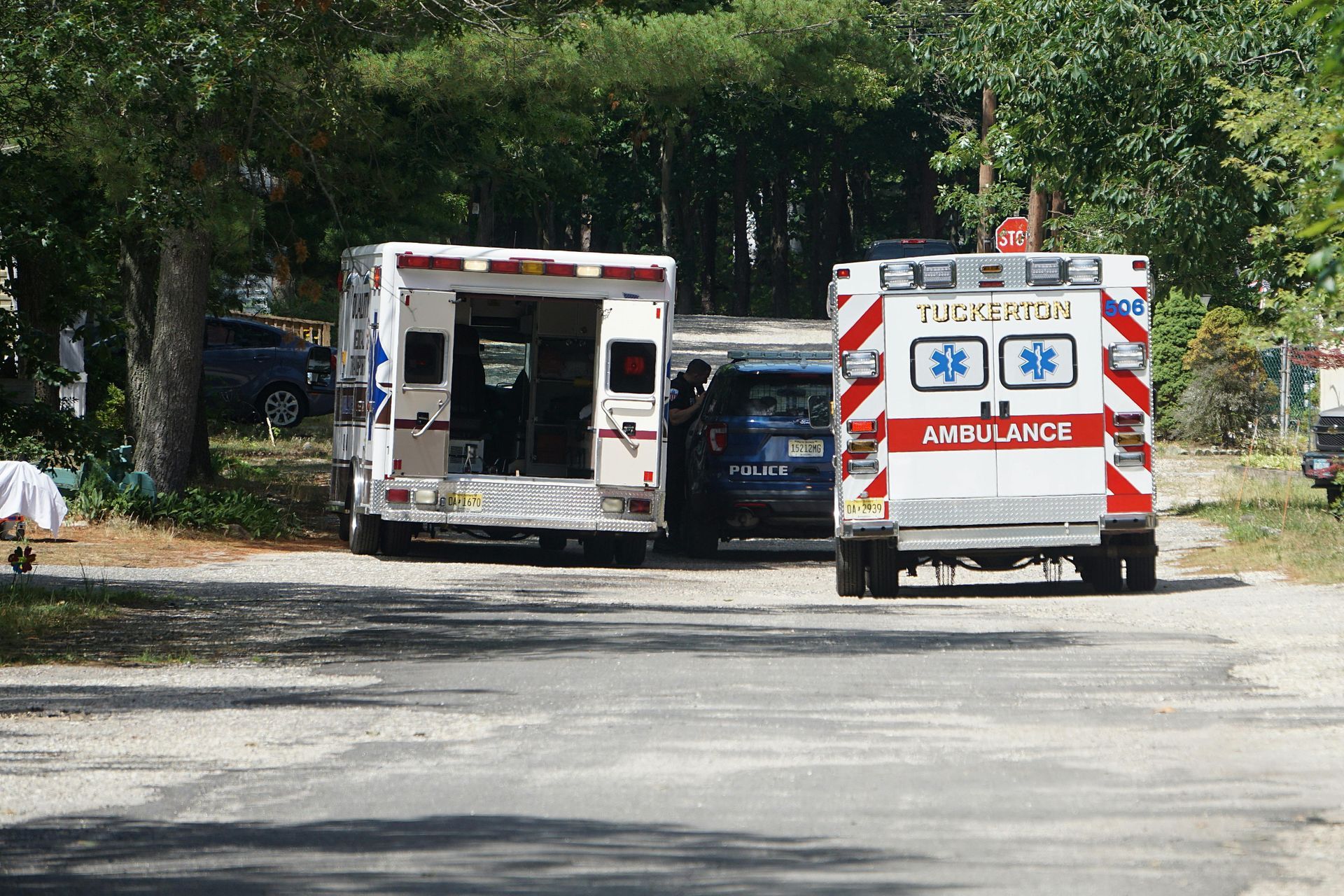 Two ambulances parked on a gravel road with a police car in between. Back doors open, emergency lights visible.
