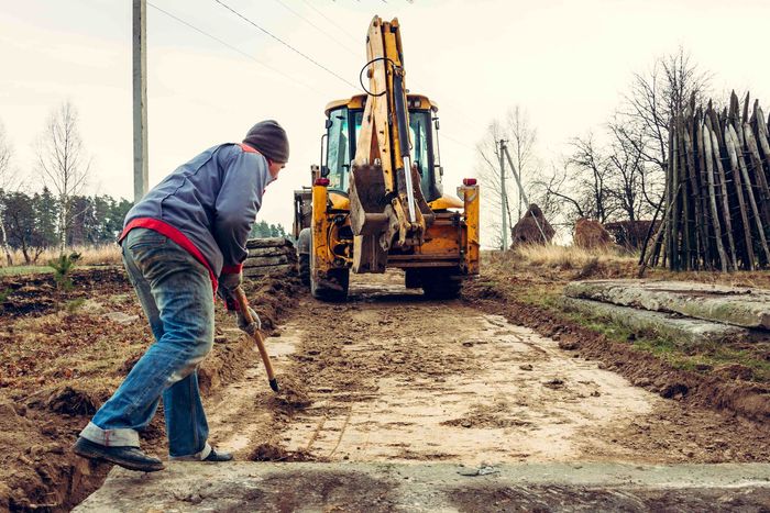 A man with a shovel grading land in front of a bulldozer