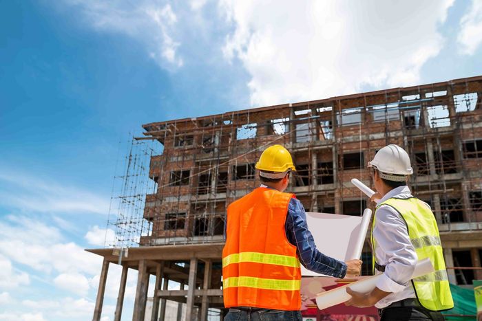 Workers planning out a demolition with papers in hand looking at the building