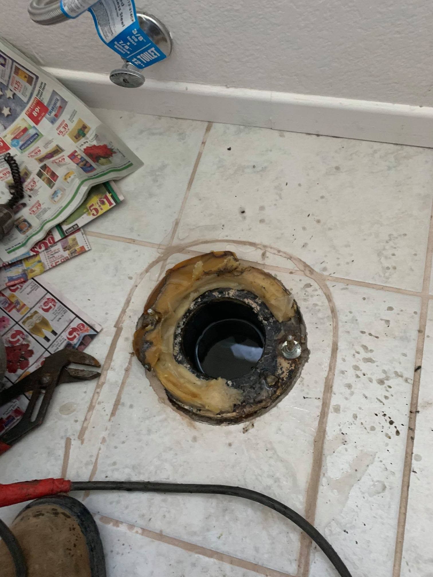 Bathroom floor with a damaged toilet flange opening and tools nearby