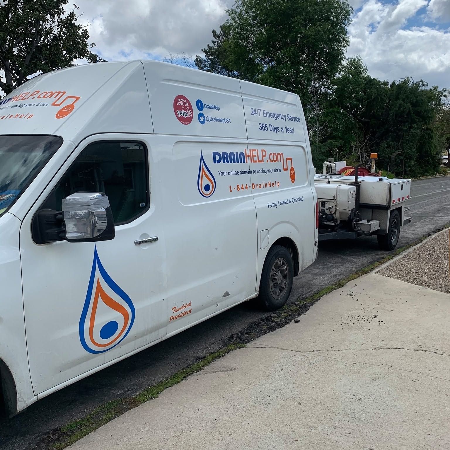 White utility van with “DRIVE” logo parked on a roadside, towing a tank trailer under cloudy skies