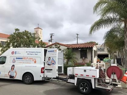 White service truck with equipment parked by a house under palm trees on a cloudy street