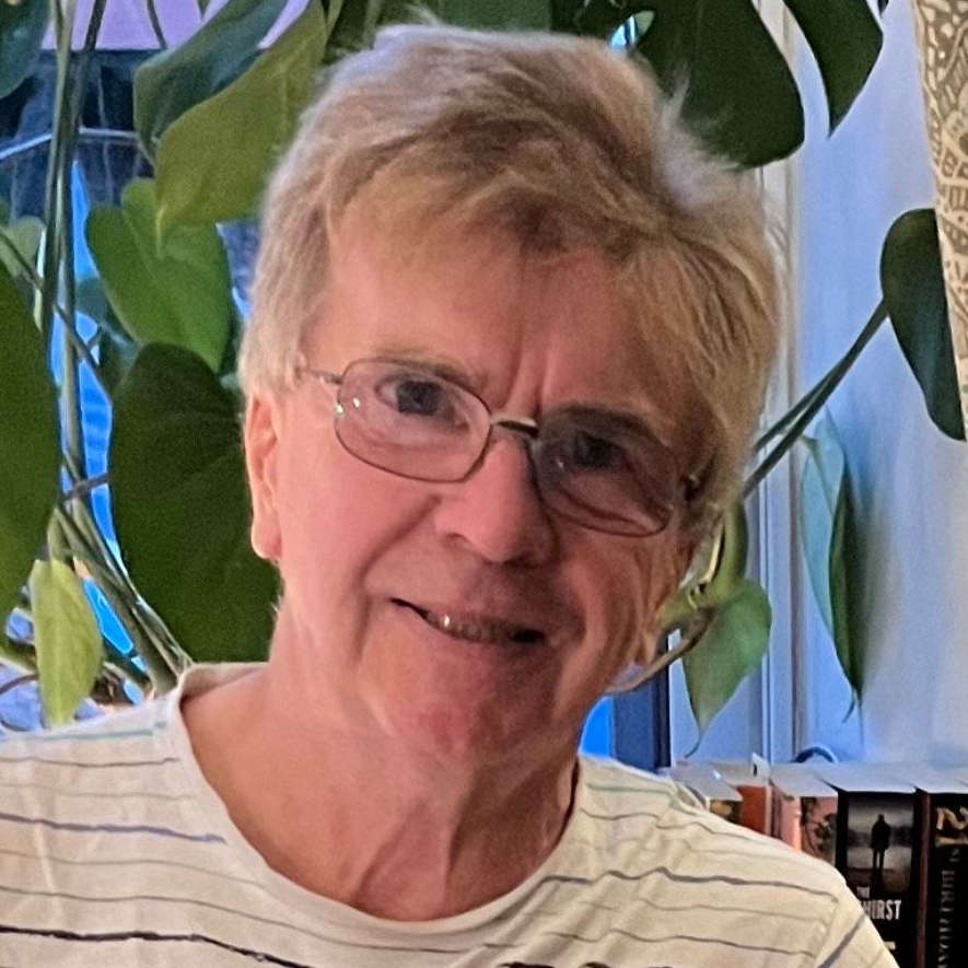 Smiling person with glasses in a leafy indoor setting