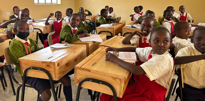 Four smiling African school children in blue sweaters, arm around shoulder.