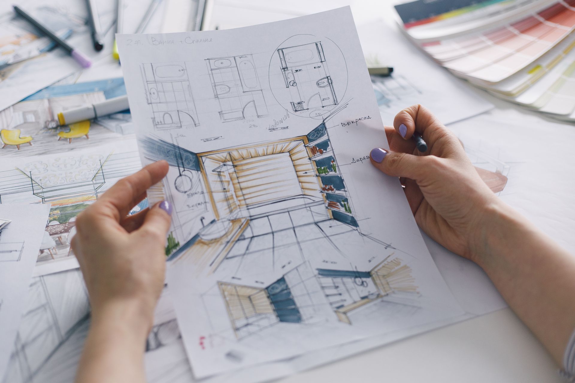 Hands holding an architectural floor plan with sketches and color swatches on a desk