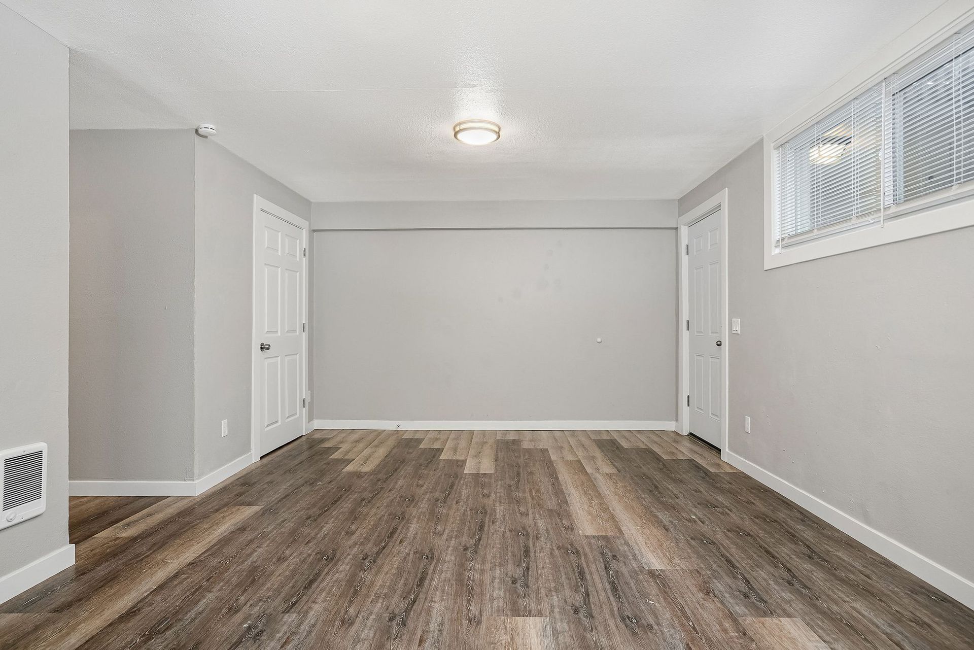 Empty gray room with wood-look flooring, white trim, and a small high window.