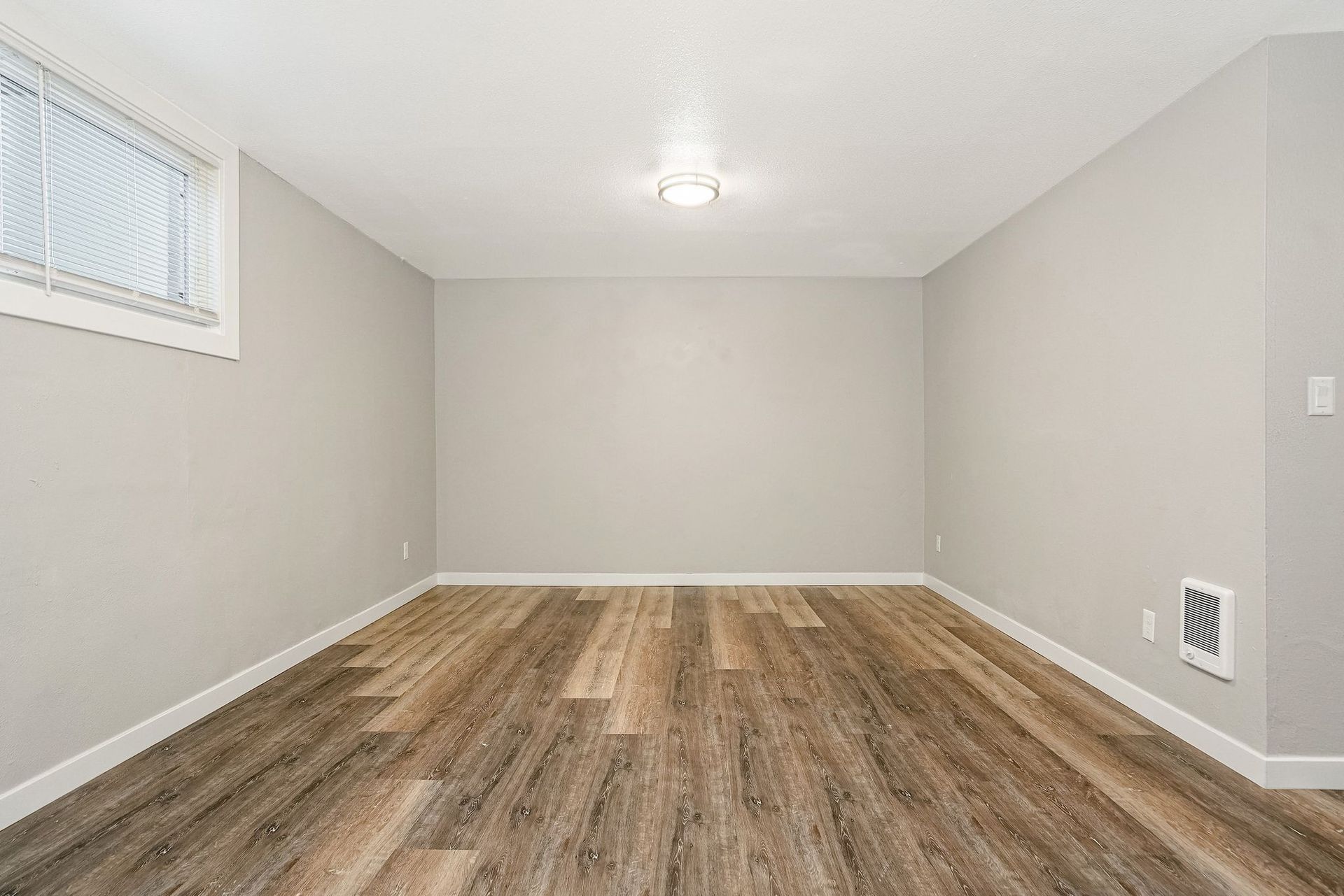 Empty beige room with wood-look flooring, small window, and ceiling light