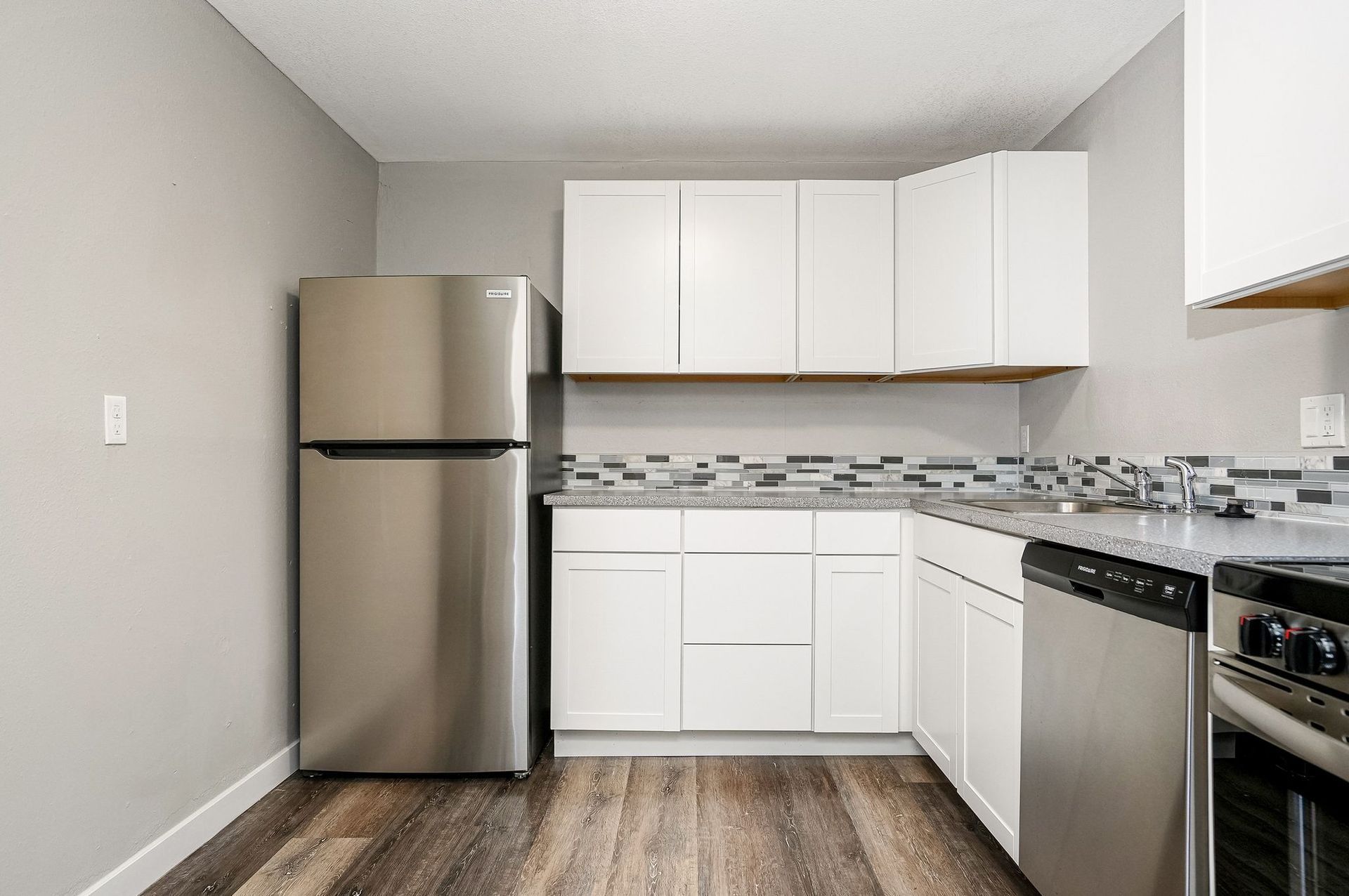 Modern kitchen with stainless steel refrigerator, white cabinets, and patterned backsplash
