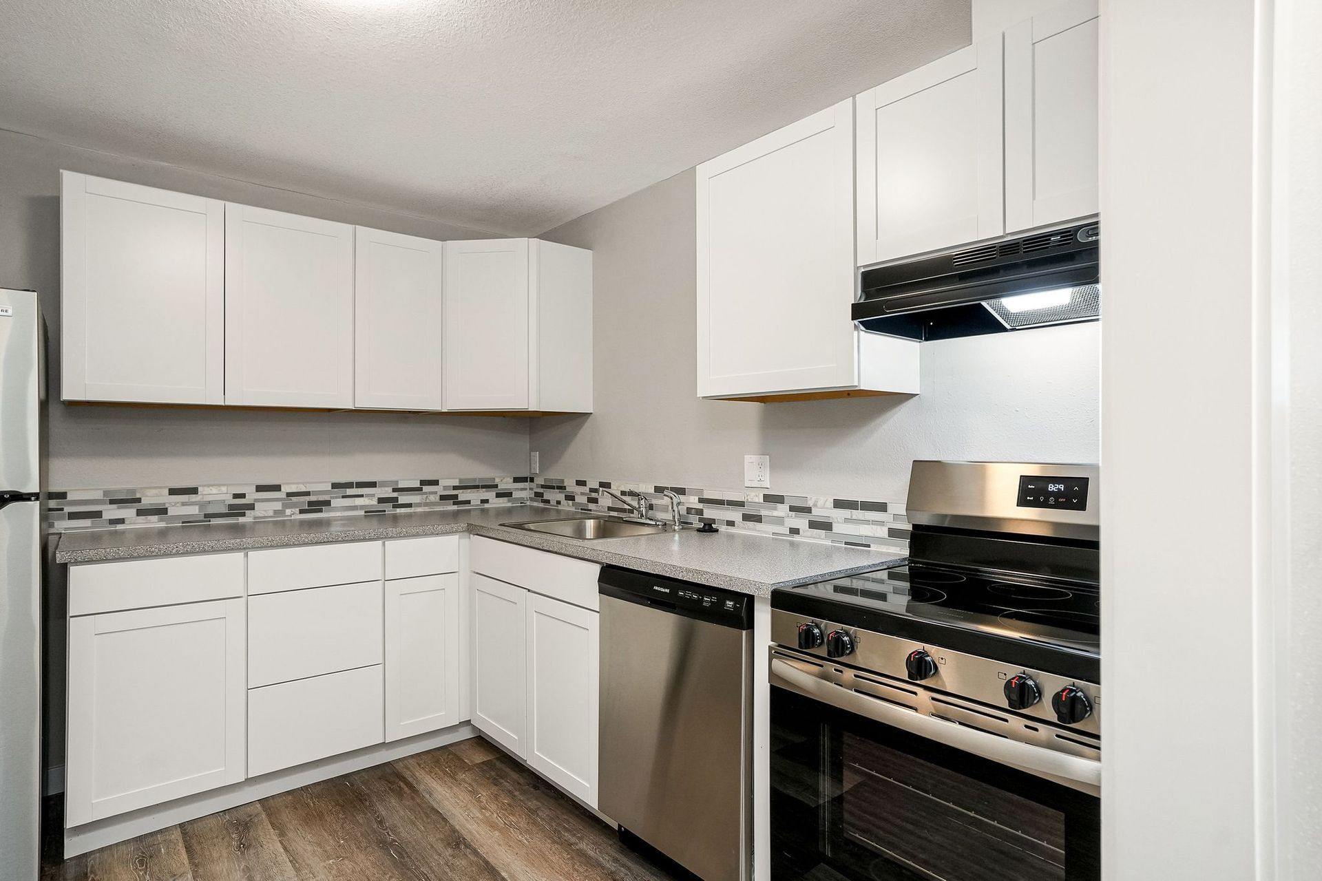 Bright white kitchen with upper cabinets, gray backsplash, stainless dishwasher, and gas stove