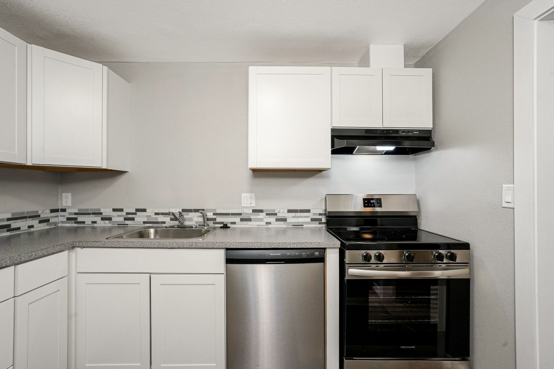 Modern kitchen with white cabinets, stainless steel appliances, and tiled backsplash