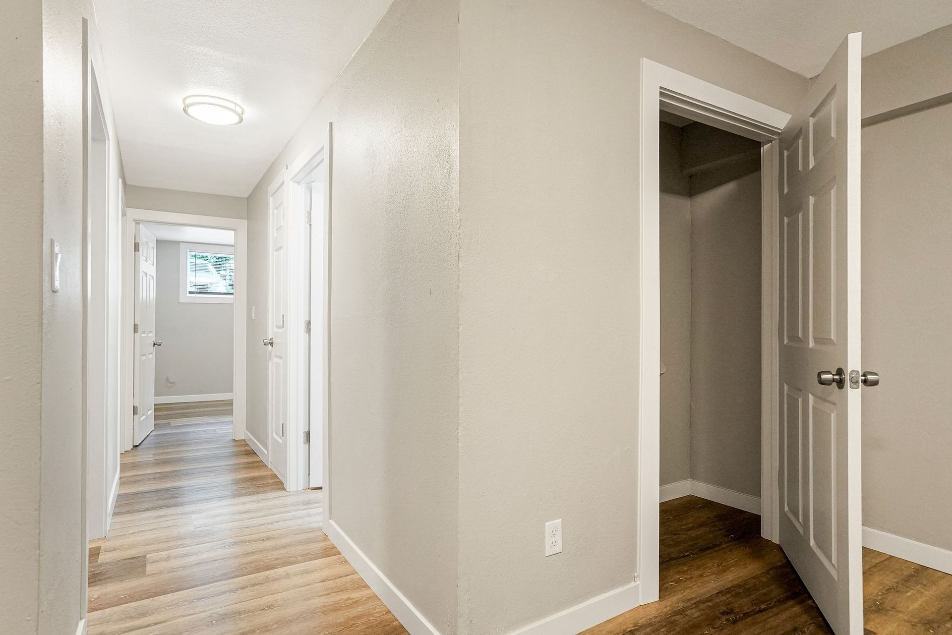 Bright hallway with white doors, beige walls, and wood flooring; open closet door on the right.