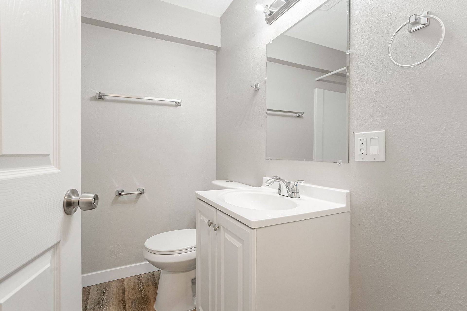Small bathroom with white vanity, toilet, mirror, and gray walls.