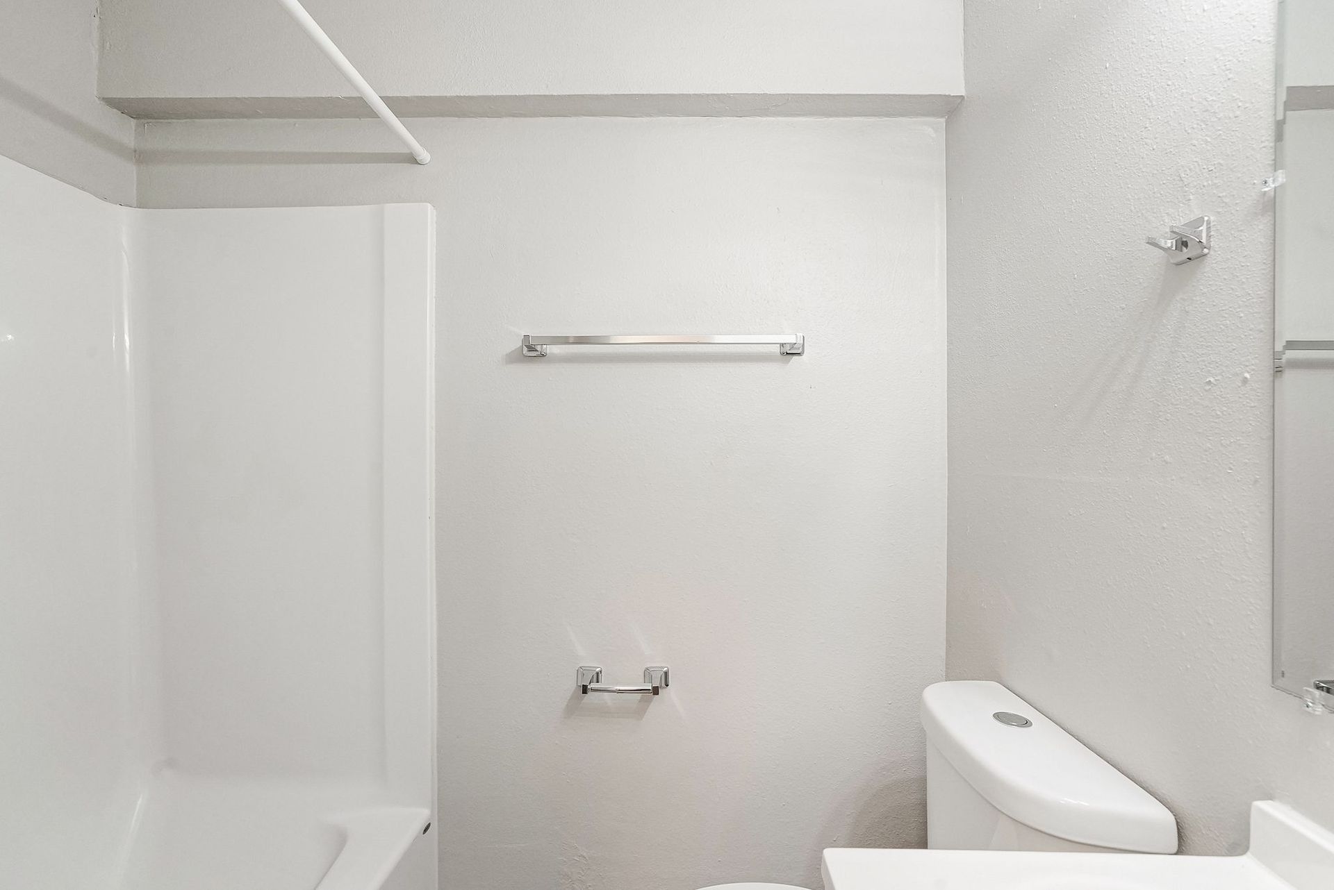 Small white bathroom with tub, towel bar, and toilet visible.