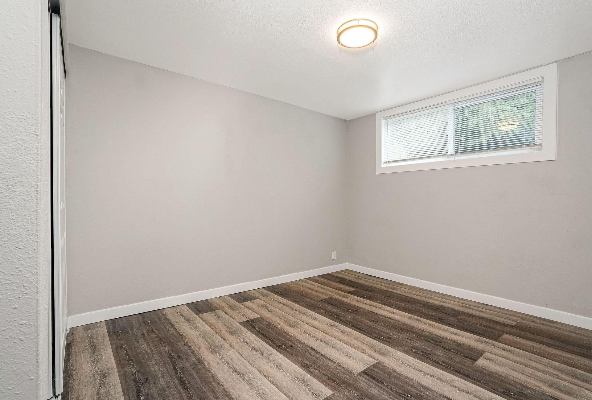 Empty room with gray walls, wood-look flooring, and a small window near the ceiling.
