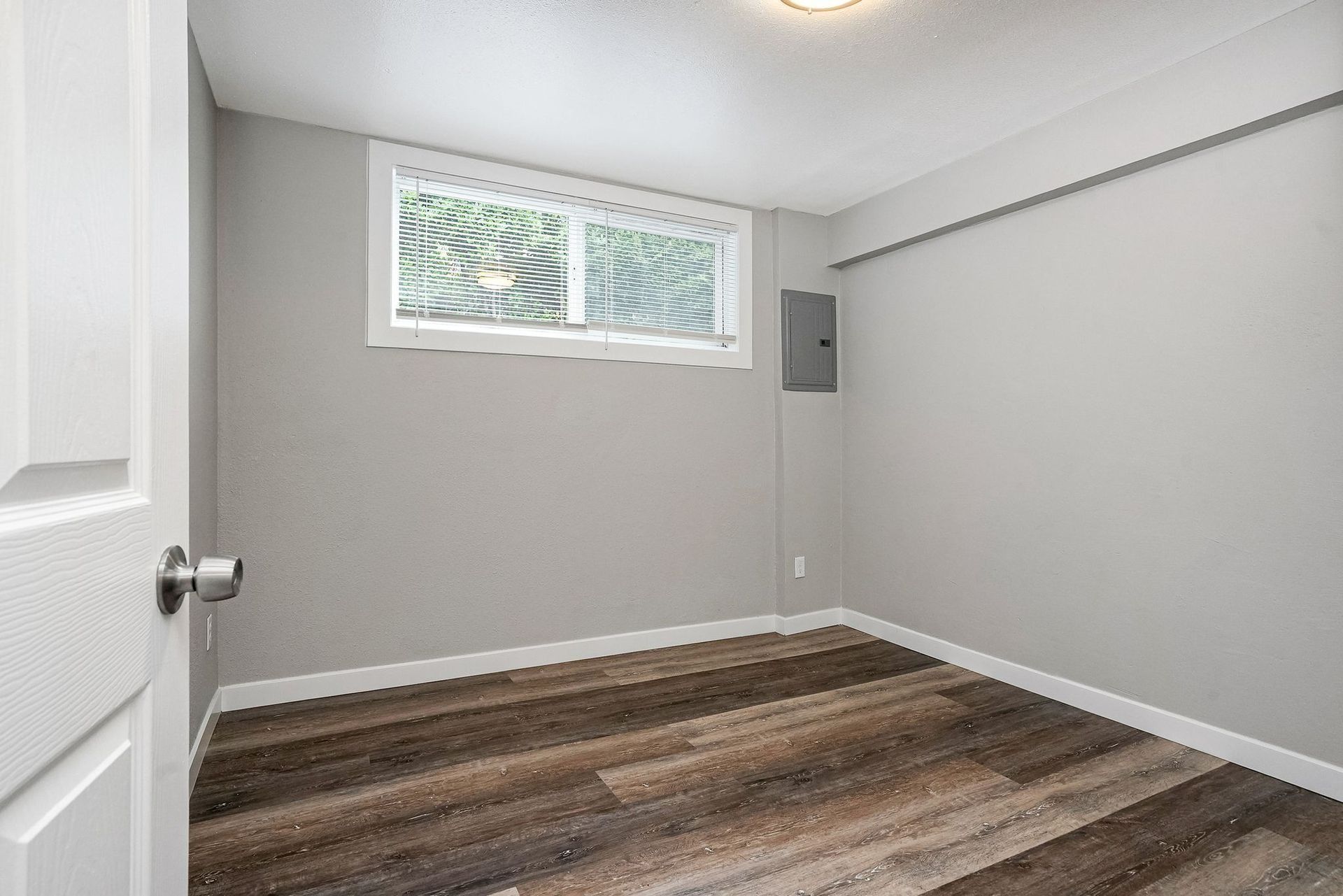Empty gray bedroom with wood flooring, white trim, and a small window.