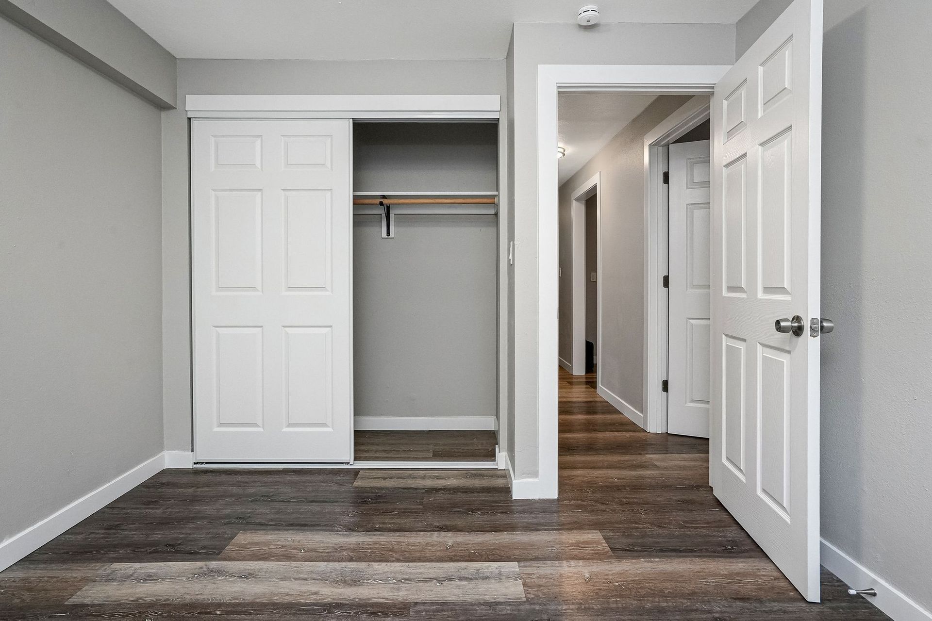Empty bedroom with open closet, gray walls, and wood-look flooring