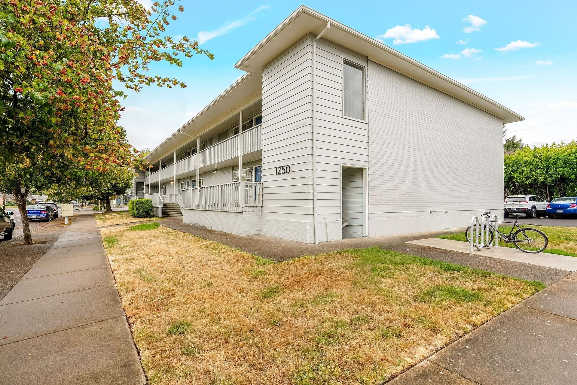 Apartment building beside a sidewalk and dry grass under a cloudy sky