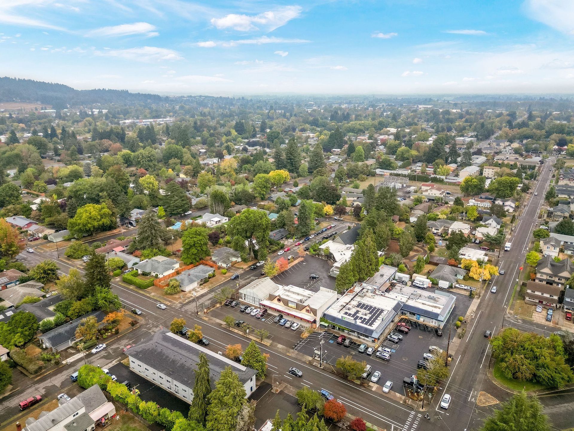 Aerial view of a suburban neighborhood with houses, trees, roads, and shops on a hazy day