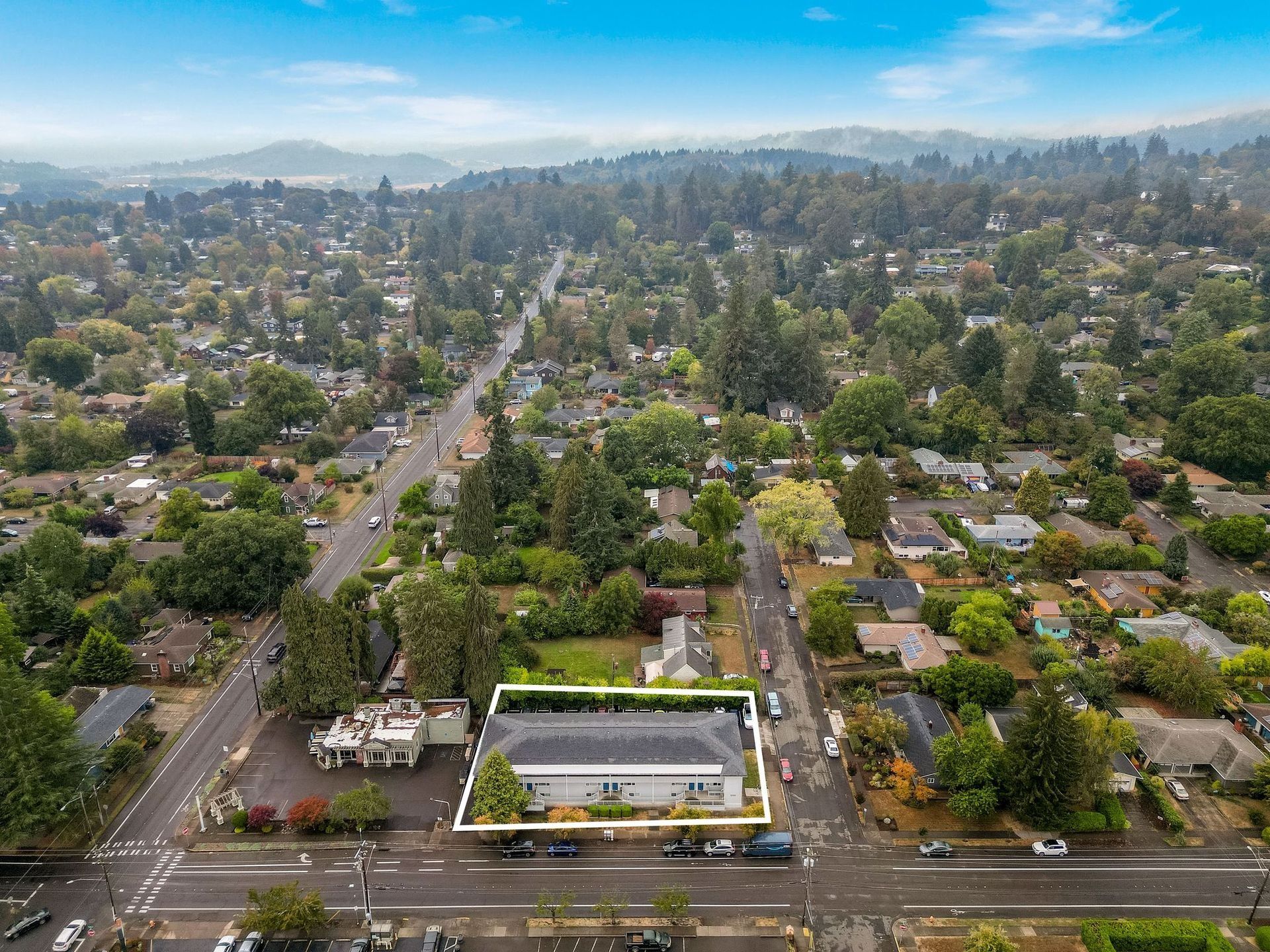 Aerial view of a suburban neighborhood with tree-lined streets and a central building near a busy road.