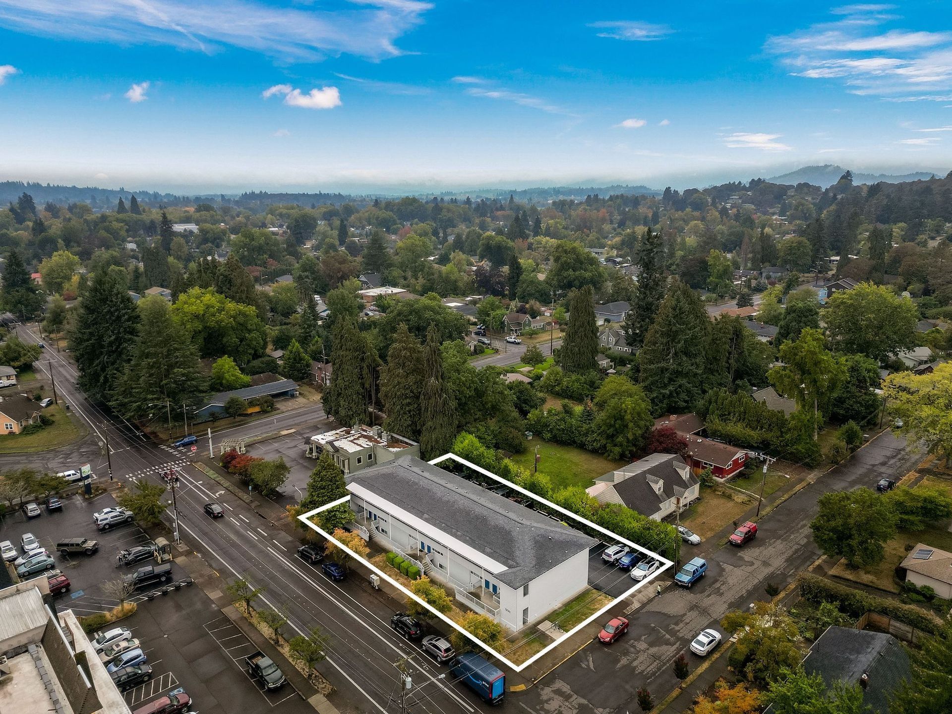 Aerial view of a white building with a highlighted roof, surrounded by streets, cars, and dense green neighborhoods.