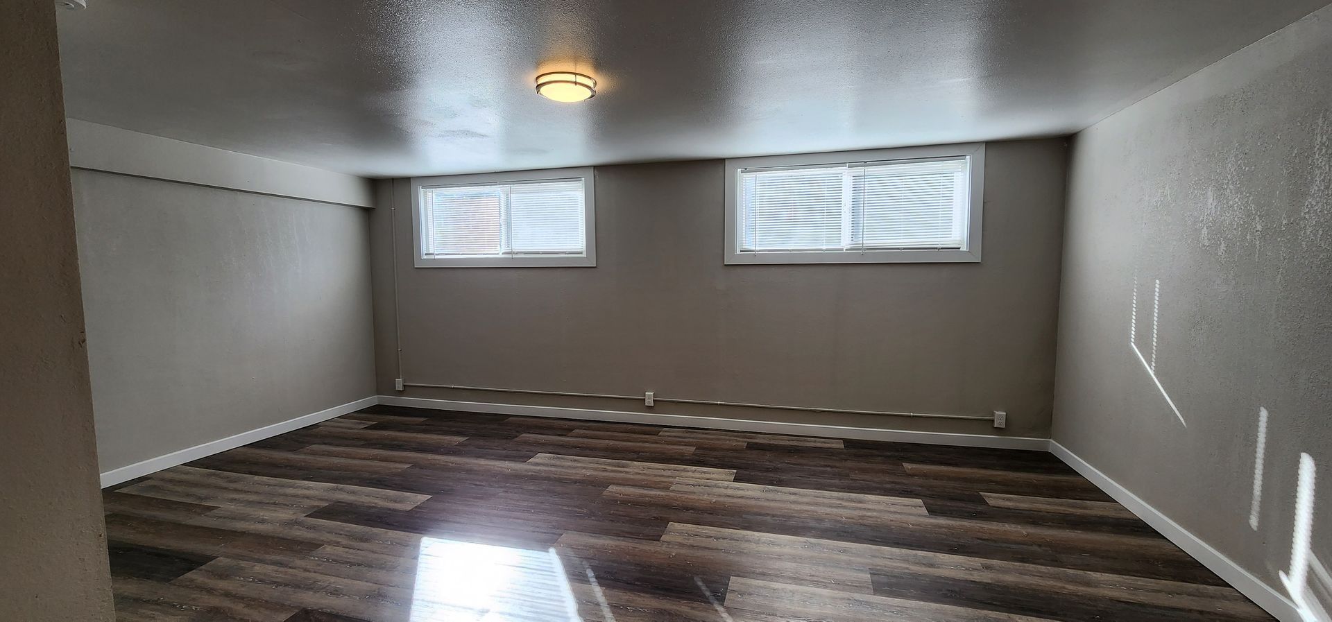 Empty beige room with dark wood floors, two small windows, and a ceiling light.