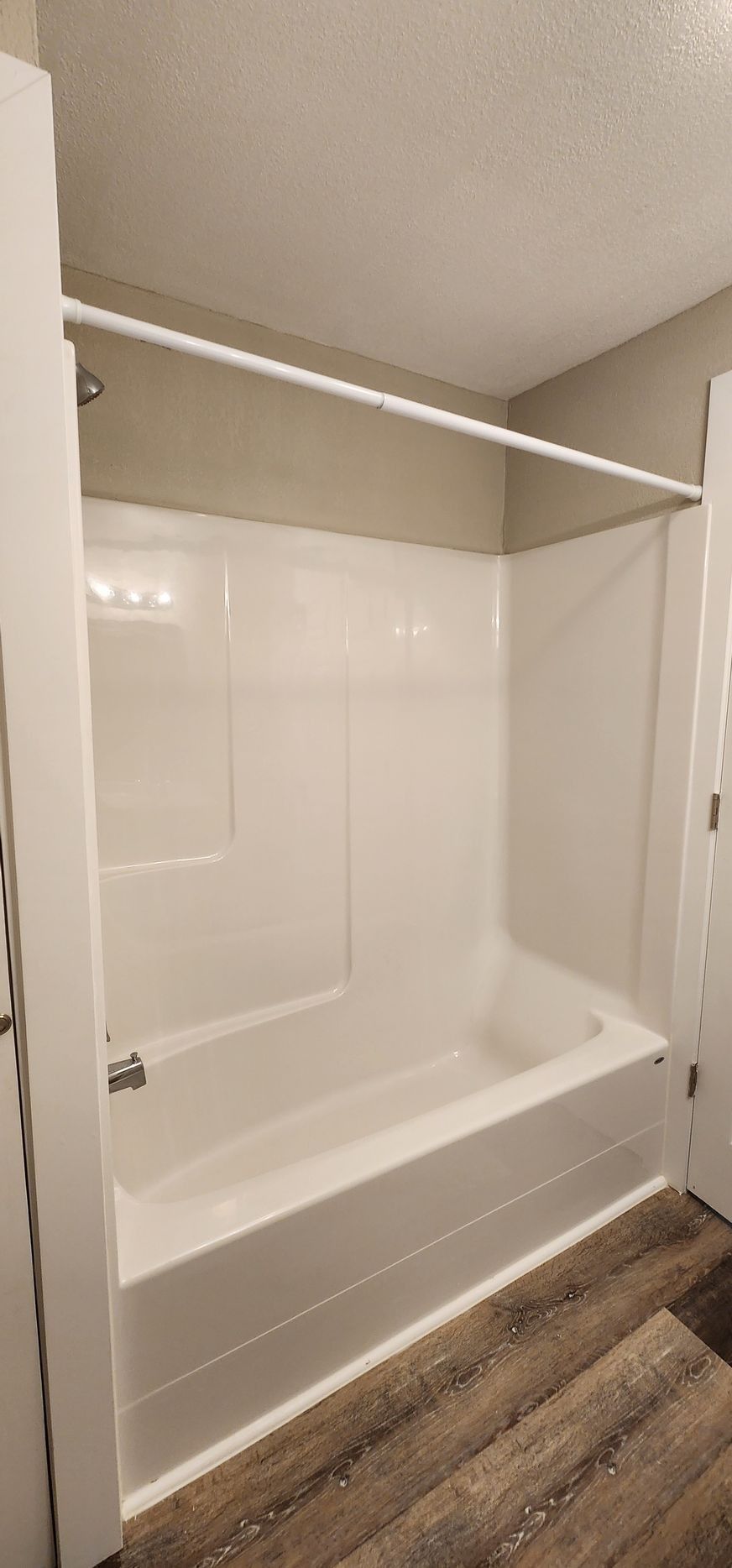 Modern bathroom with a white bathtub, tiled shower surround, and wood-look floor.