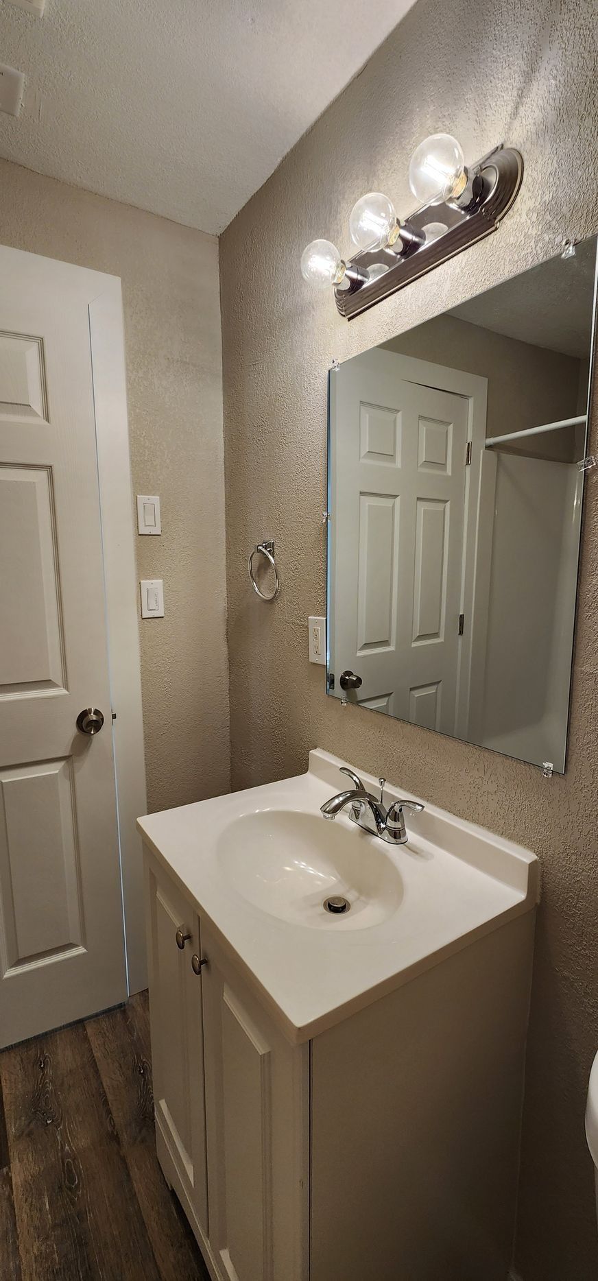 Small bathroom vanity with sink, mirror, and wall light beside a closed door.