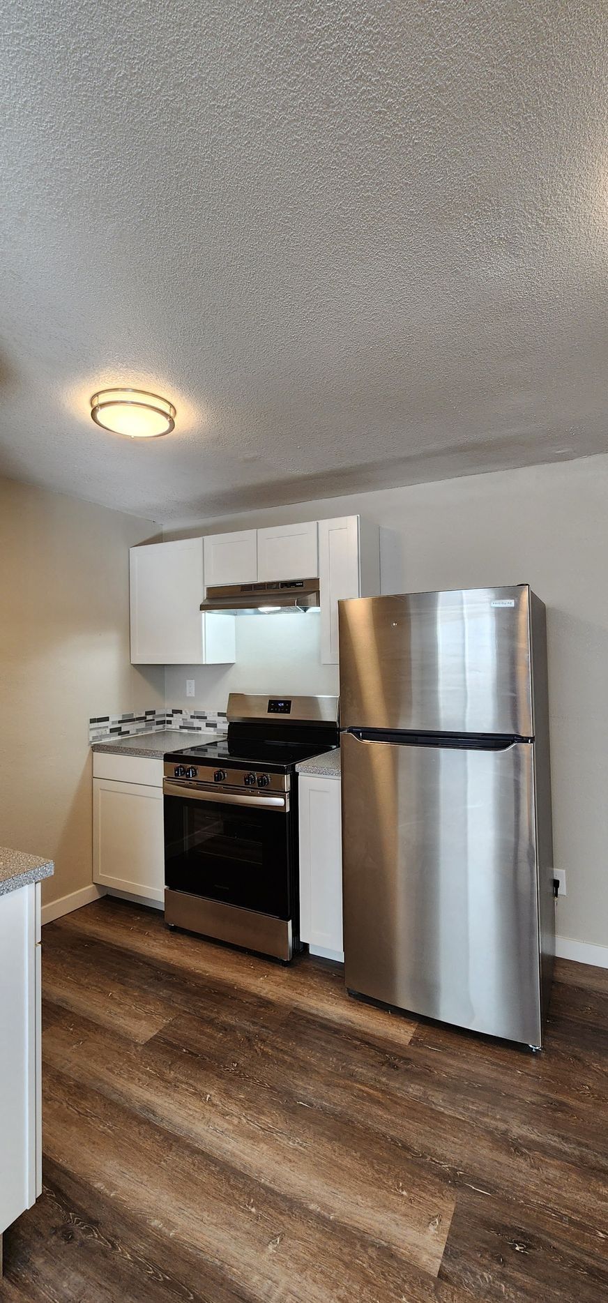 Small kitchen with stainless steel fridge, stove, and white cabinets on wood flooring.