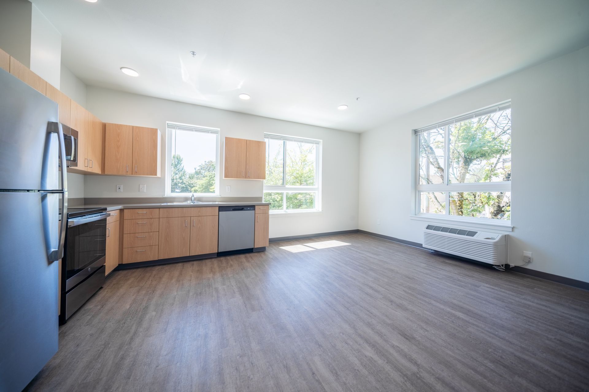 Empty modern kitchen with wood cabinets, stainless appliances, large windows, and gray flooring