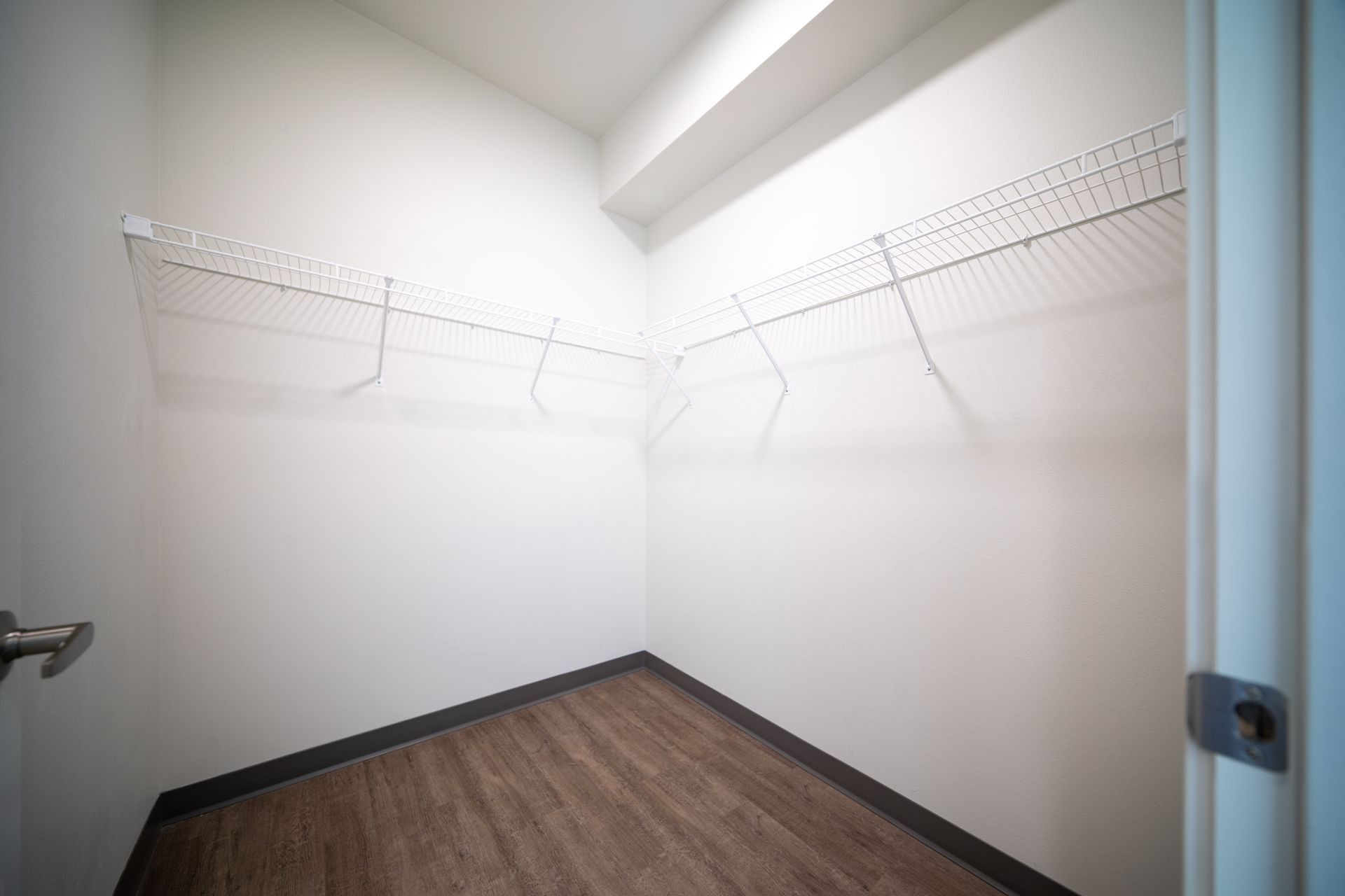 Empty walk-in closet with white walls, wire shelves, and wood-look flooring.