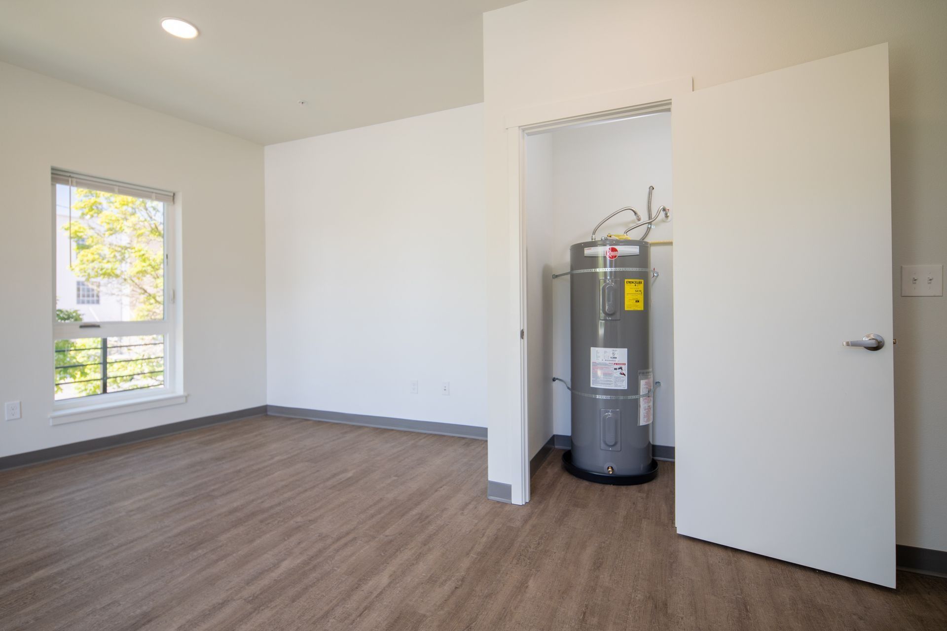 Empty room with wood floor, white walls, and an open utility closet showing a water heater.