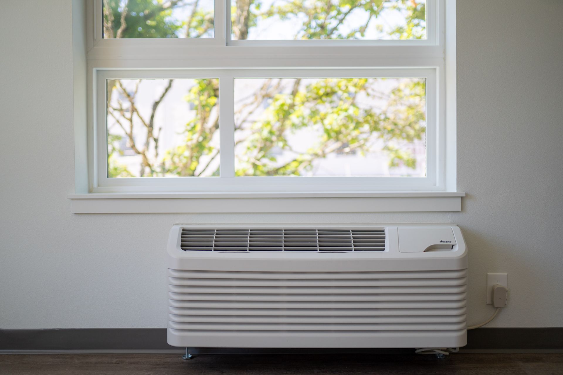 White window air conditioner beneath a sunlit window in a bright room