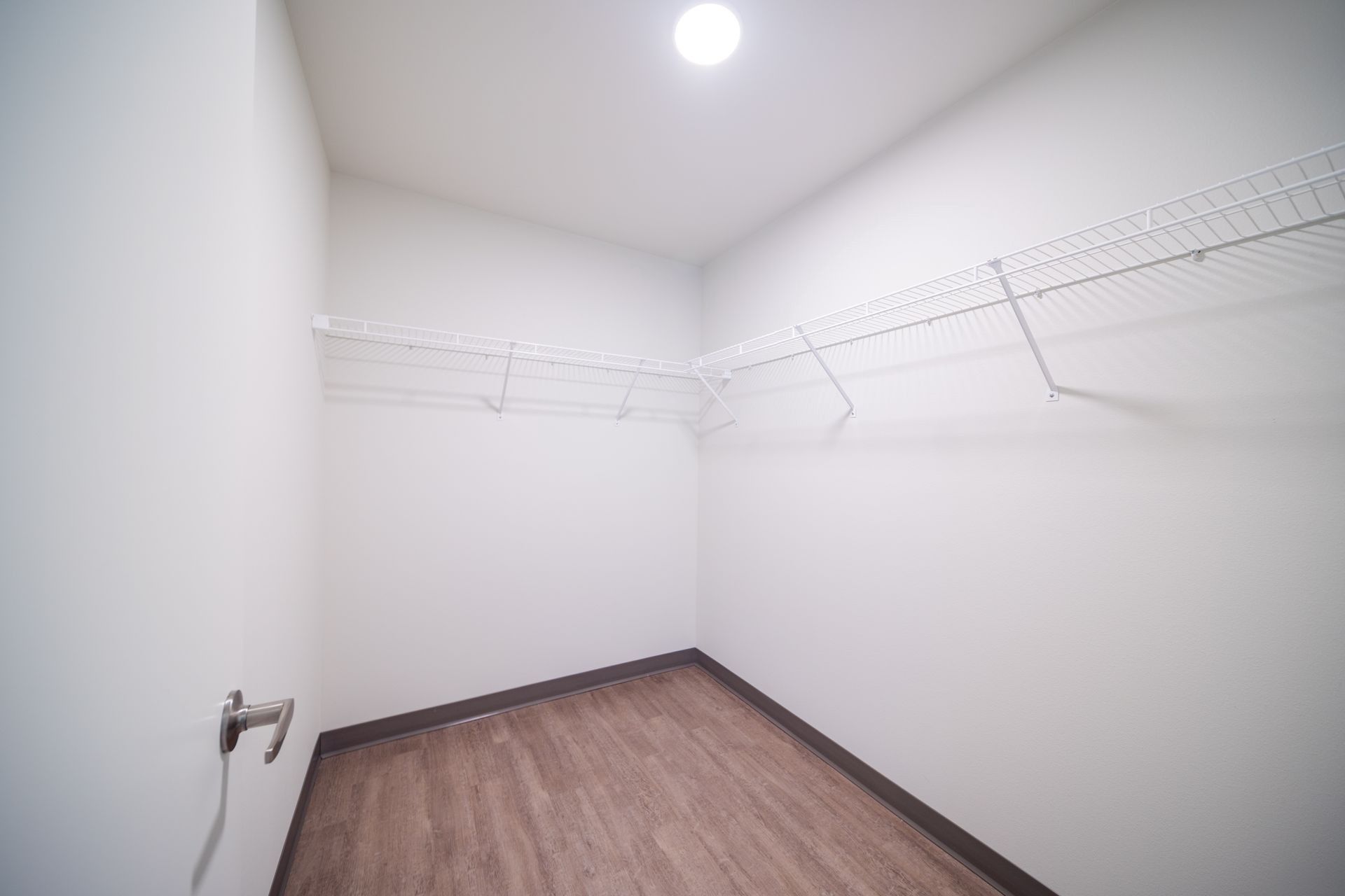 Empty white walk-in closet with wood floor and hanging racks along the walls