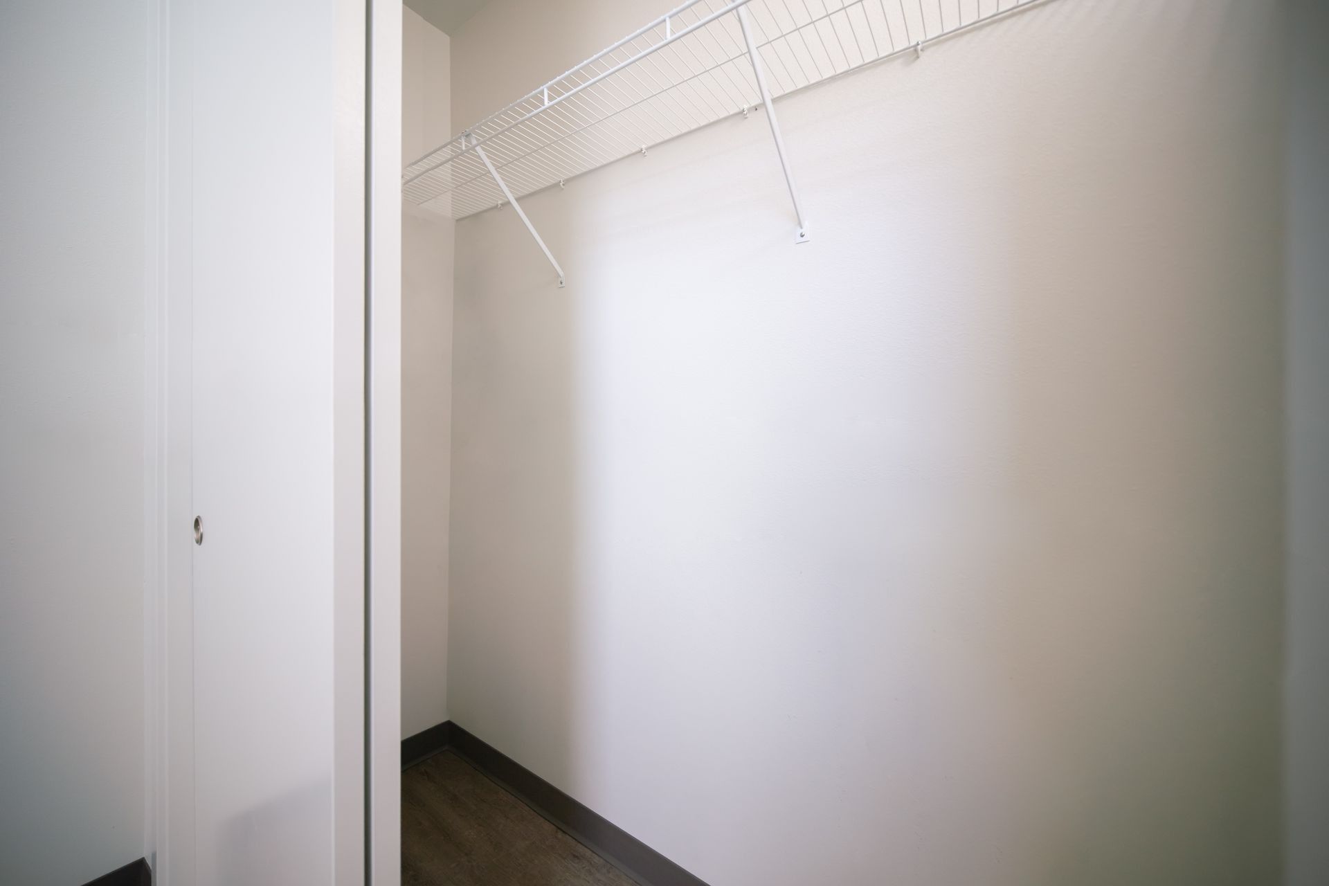 Empty white closet with wire shelving and dark floor trim