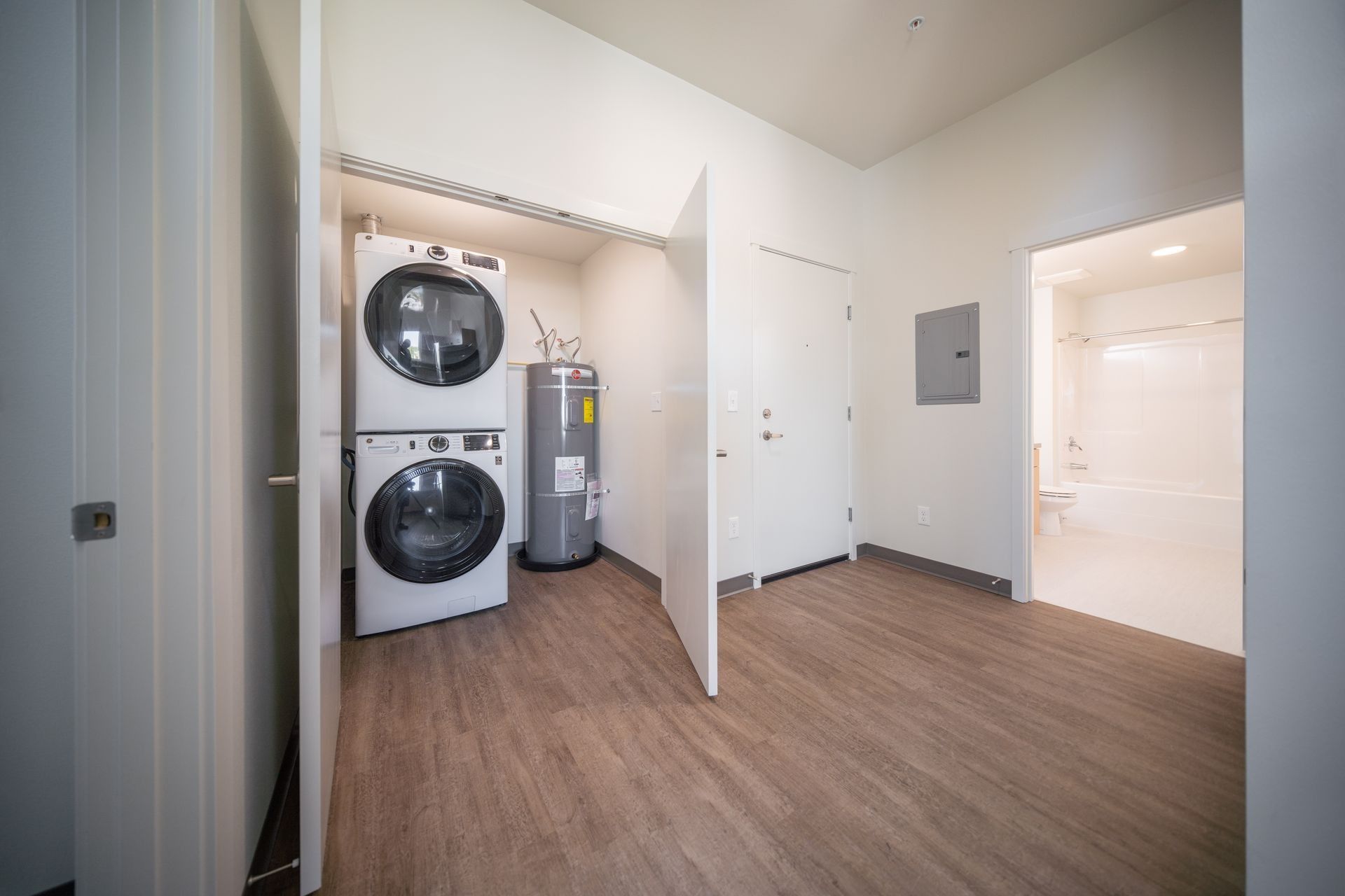 Laundry room with stacked washer and dryer, utility sink, and wood-look flooring in a bright apartment hallway