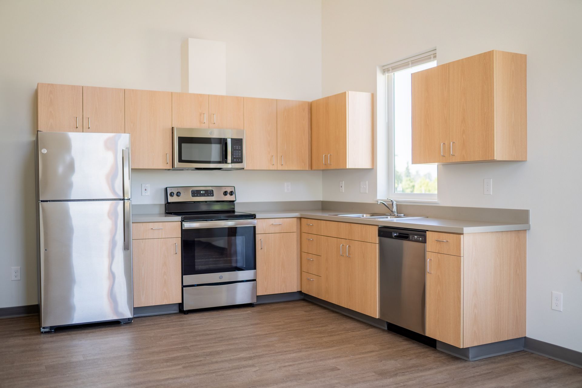 Modern kitchen with stainless steel appliances, light wood cabinets, and gray countertops