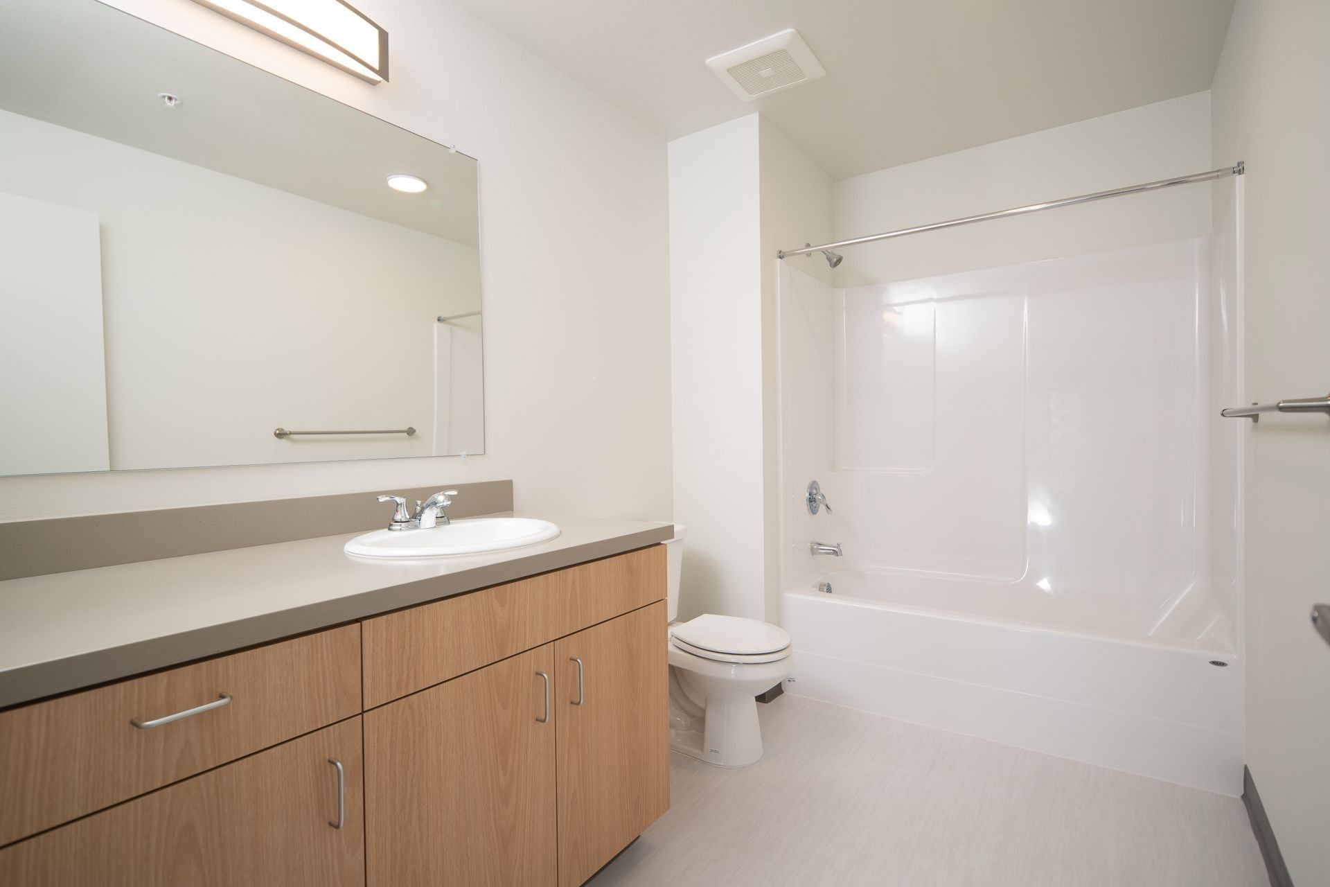 Modern bathroom with double vanity, large mirror, toilet, and white tub shower.