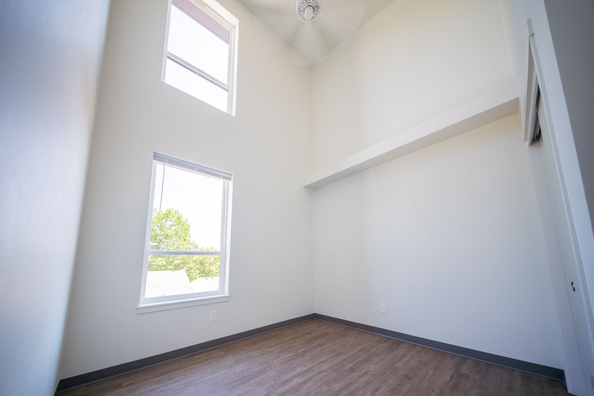 Bright empty room with white walls, two windows, and wood flooring.