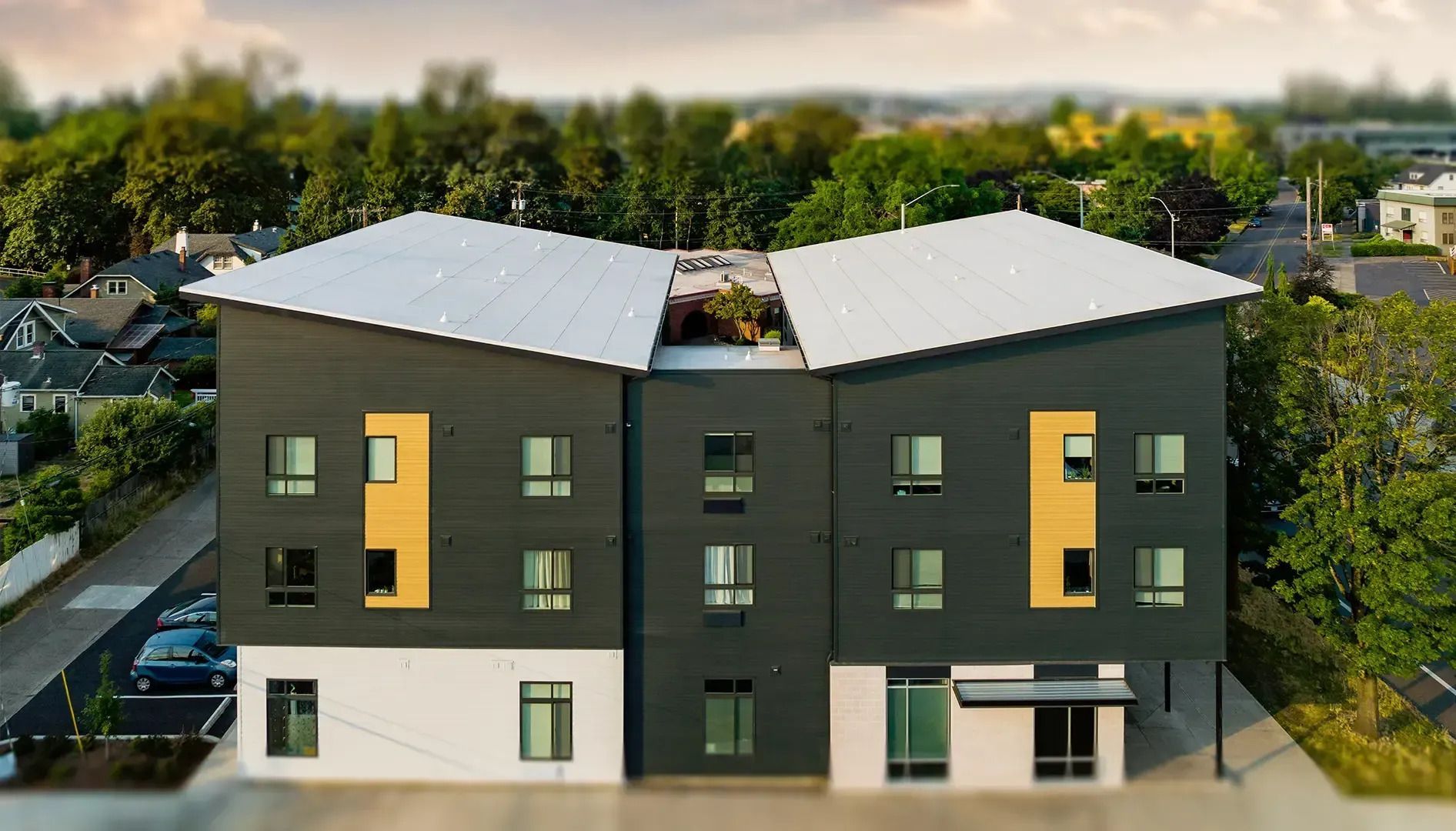 Modern dark-gray apartment building with yellow accents and rooftop solar panels, viewed from above.