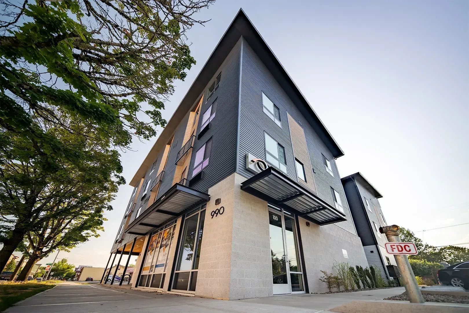 Modern two-story corner building with black awnings and large glass windows in a sunny street setting